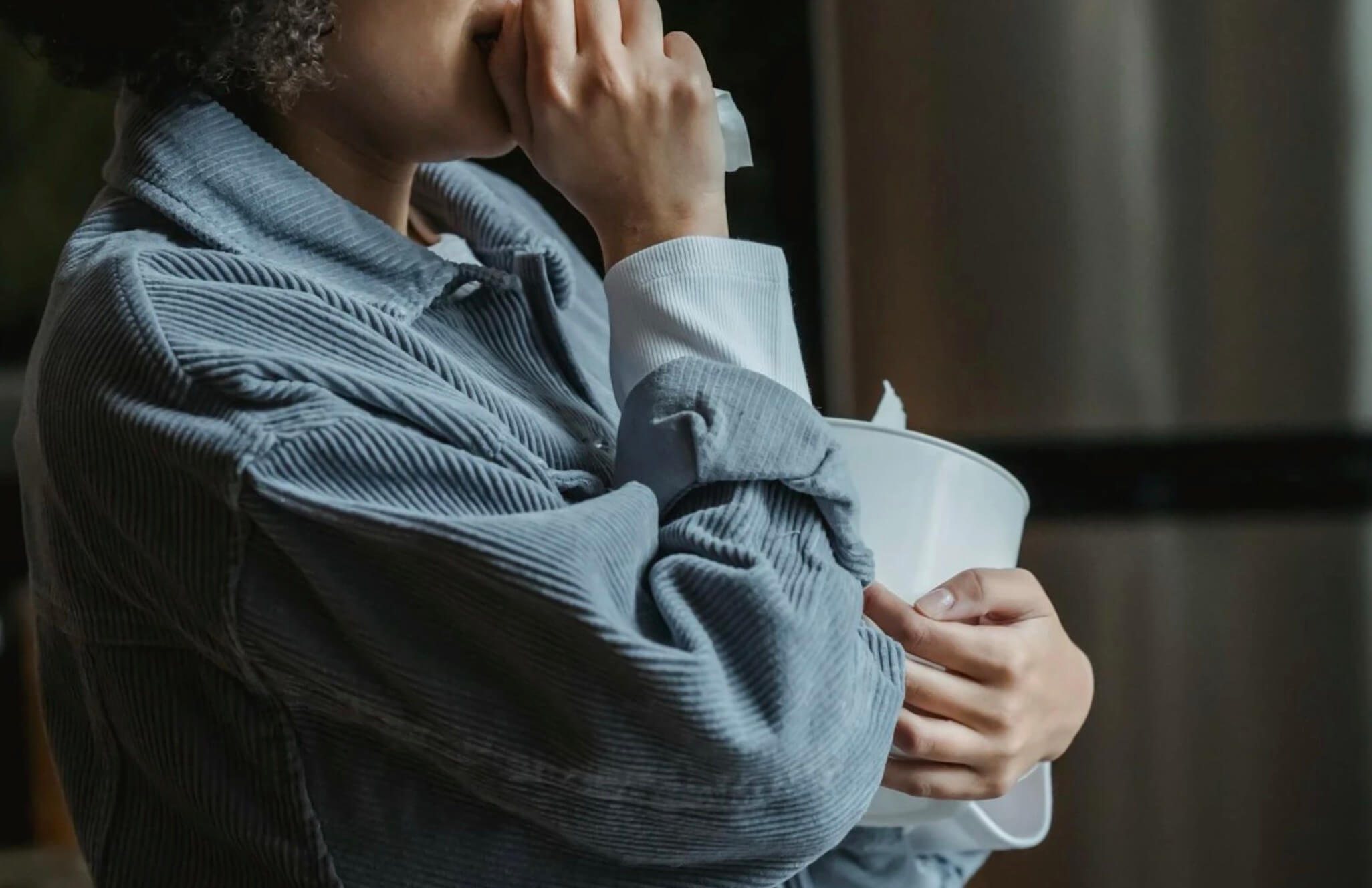 Person wiping tears while holding a tissue and a bowl